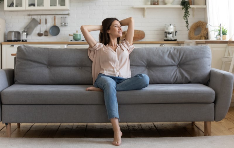 Mulher feliz sentada no sofá de casa | Conforto térmico | Método Construtivo | Blog Alea