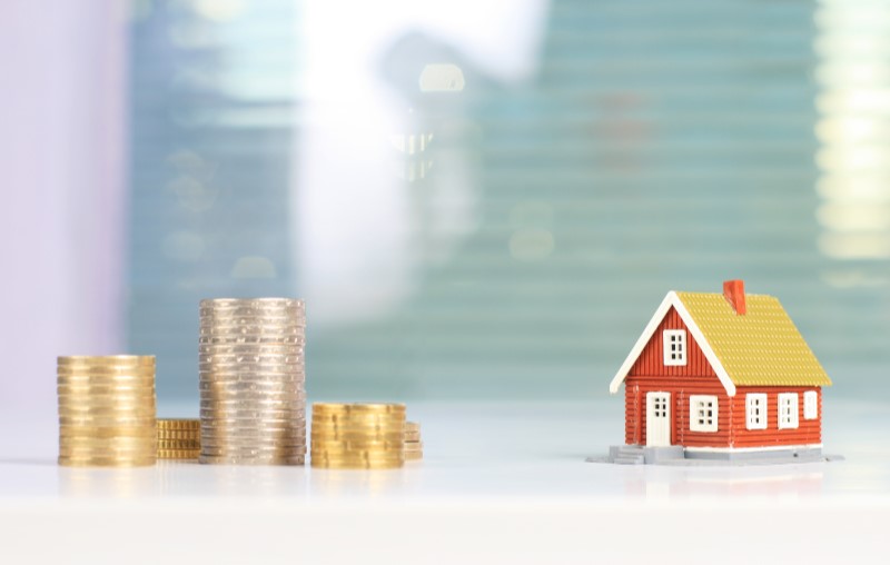 Como financiar um imóvel | Moedas empilhadas e uma miniatura de casa | Como comprar uma casa | Blog Alea