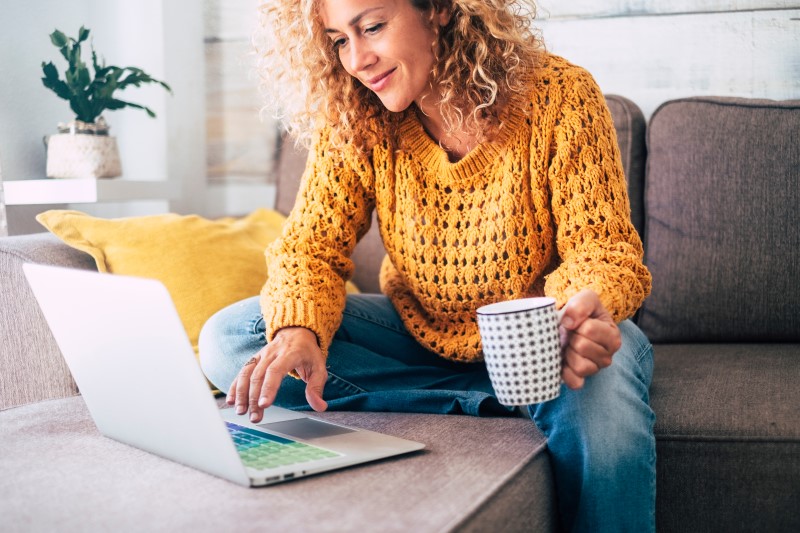 Quais são os benefícios do Casa Verde e Amarela | Foto de uma mulher feliz pesquisando na internet e tomando café | Tudo sobre o Casa Verde e Amarela | Blog Alea