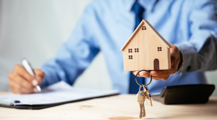 Análise de crédito | Um corretor de imóveis segurando uma miniatura de casa de madeira e assinando um contrato | Como comprar uma casa | Blog Alea