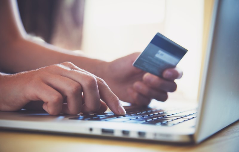 Débito automático | Pessoa segurando um cartão de crédito enquanto pesquisa na internet | Como comprar uma casa | Blog Alea