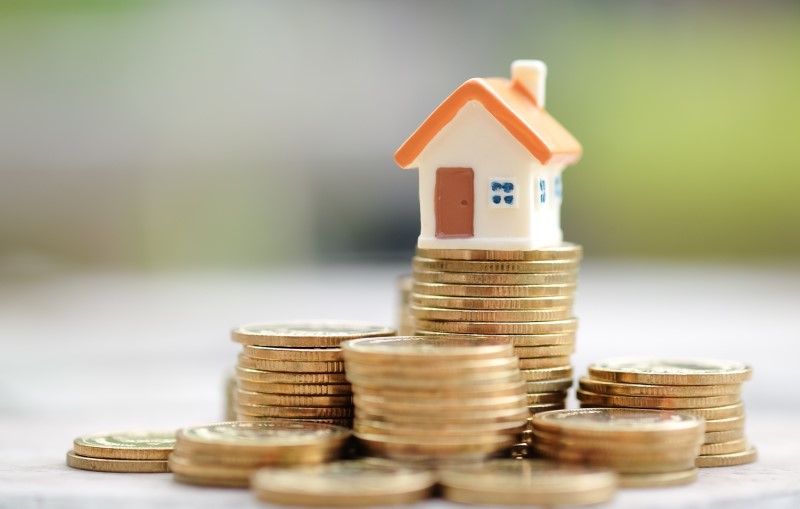 O que são juros de obra | Foto de uma miniatura de casa e moedas empilhadas | Como comprar uma casa | Blog Alea