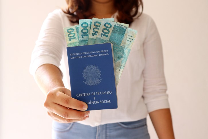 Décimo terceiro para financiar casa | Foto de uma mulher segurando a Carteira de Trabalho com dinheiro | Como comprar uma casa | Blog Alea