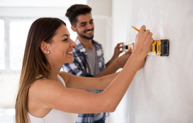 O que deve ser avaliado durante a vistoria de imóvel | Foto de um casal medindo a parede | Como comprar uma casa | Blog Alea