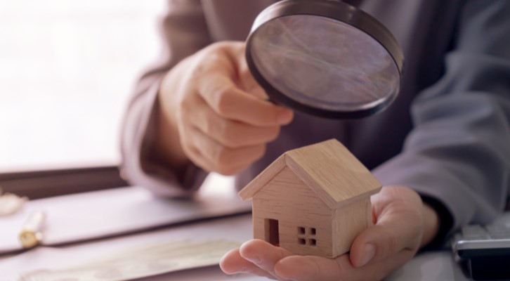 Vistoria de imóvel | Foto de uma pessoa segurando uma lupa analisando uma miniatura de casa | Como comprar uma casa | Blog Alea