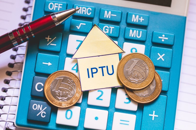 O que é o Imposto Predial Territorial Urbano | Foto de moedas em cima de uma calculadora e caneta com a palavra IPTU | Como comprar uma casa | Blog Alea