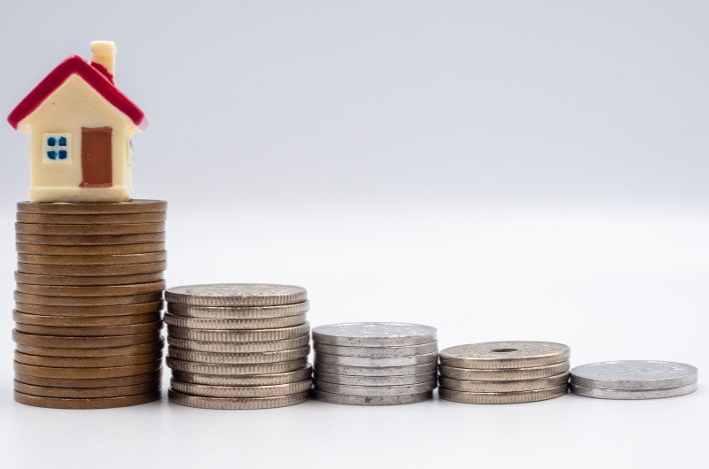 Como funciona o subsídio para comprar um imóvel | Foto de moedas organizadas em uma fileira, com uma miniatura de casinha no topo | Tudo sobre Minha Casa Minha Vida | Blog da Alea