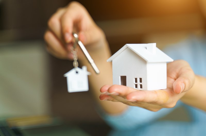 Como juntar dinheiro para comprar um imóvel ganhando pouco? | Foto de uma pessoa segurando uma miniatura de casa e uma chave com chaveiro de casinha | Blog Alea
