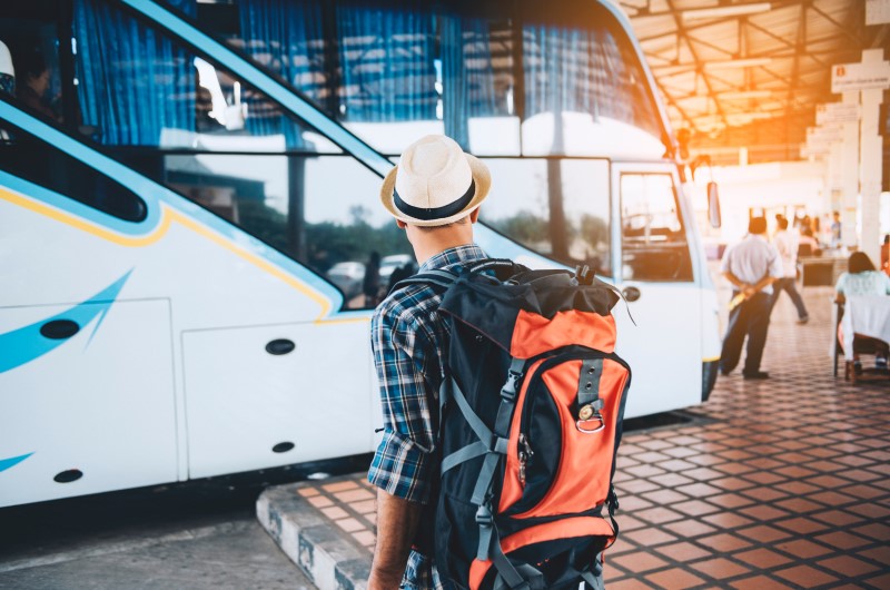 Como chegar na cidade? | Foto de um homem com uma mochila próximo a um ônibus de viagem | Estilo de vida | Blog Alea