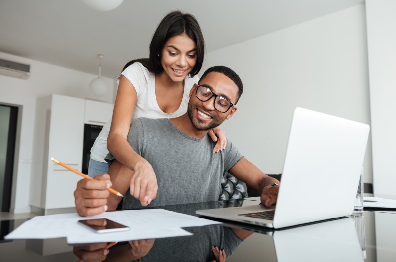 Conhecendo os principais bairros de Três Lagoas | Foto de um casal sorrindo na frente do notebook, enquanto olham para uma folha de papel | Estilo de Vida | Blog Alea