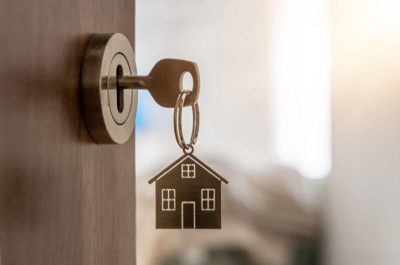 O que é preciso para adquirir a casa própria? | Foto de uma chave com chaveiro de casinha, pendurado em um fechadura | Como comprar uma casa | Blog Alea