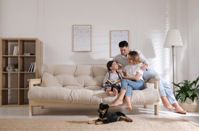 Um pouco de história | Foto de uma família feliz sentada no sofá, enquanto a filha de um casal lê um livro | Estilo de Vida | Blog Alea