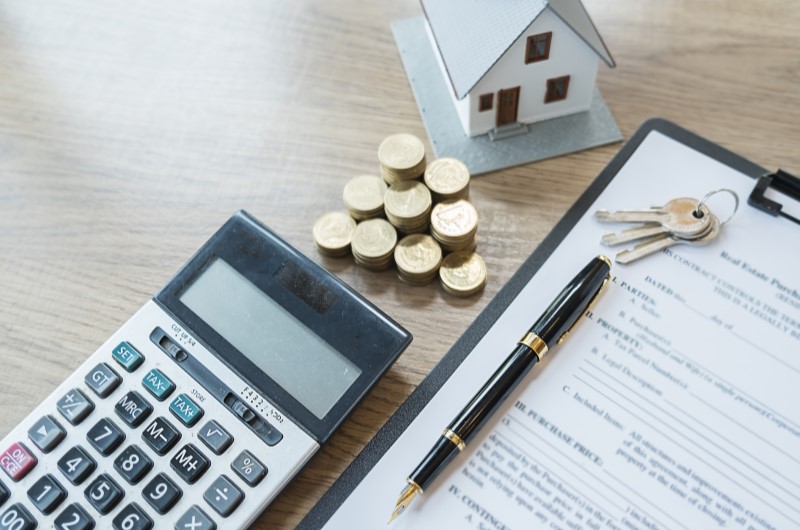 É possível usar o FGTS para financiar com a Caixa? | Foto de um documento, caneta, calculadora, moedas e uma casinha | Como comprar uma casa | Blog Alea 