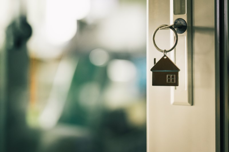 Quais são os benefícios de se inscrever no Minha Casa, Minha Vida? | Foto de uma porta entreaberta com um chaveiro de casinha na porta | Tudo sobre o Minha Casa Minha Vida | Blog Alea