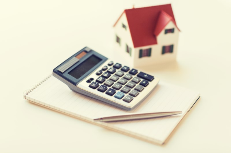 Taxas de juros menores | Foto de uma calculadora sobre um caderno, ao lado de uma casinha | Blog Alea